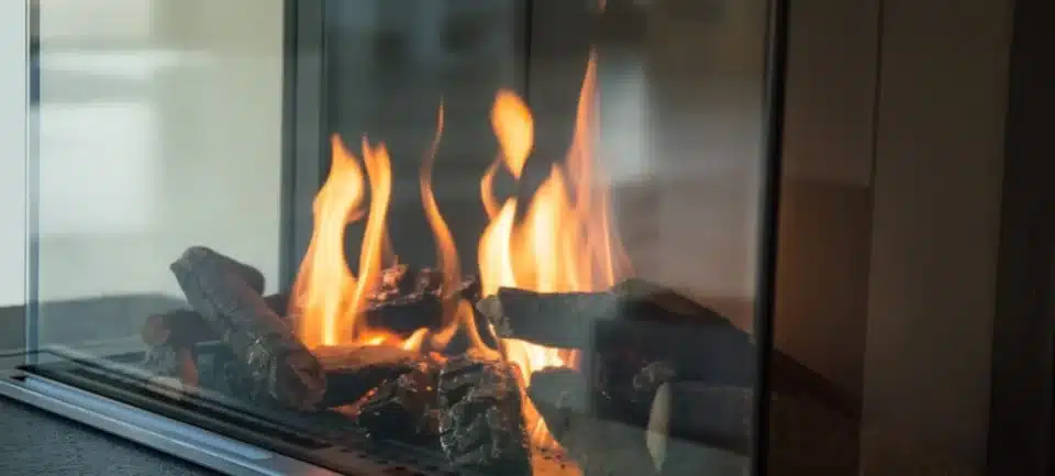 A fireplace is lit in a living room where a christmas tree is present.