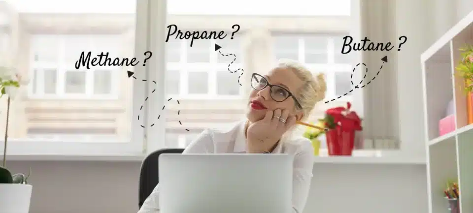 Woman sitting at desk with laptop thinking with words methane, propane and butane floating around her head.