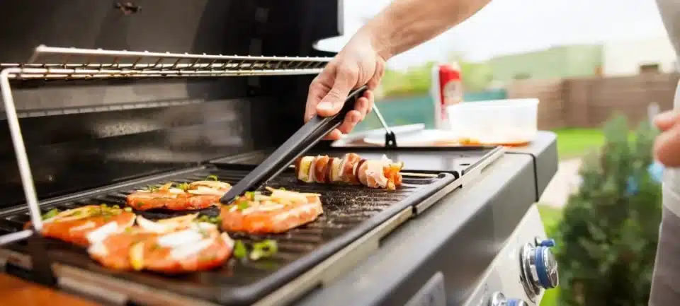 A man is holding a pair of tongues and flipping meat on a grill
