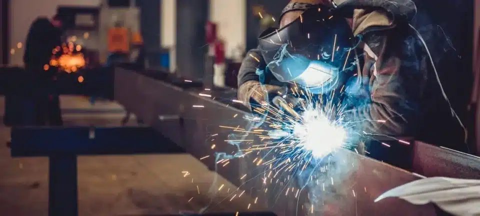 A man with a protective mask welds materials in a shop.