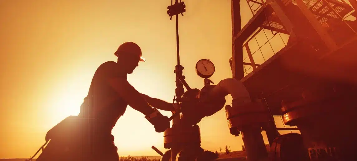 An oil worker is checking the oil pump on a sunset background.