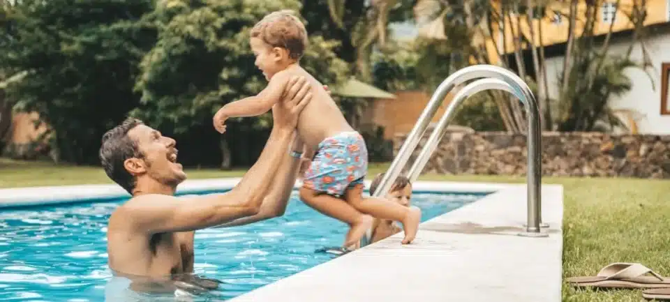 Father helping small toddler jumping into the pool.
